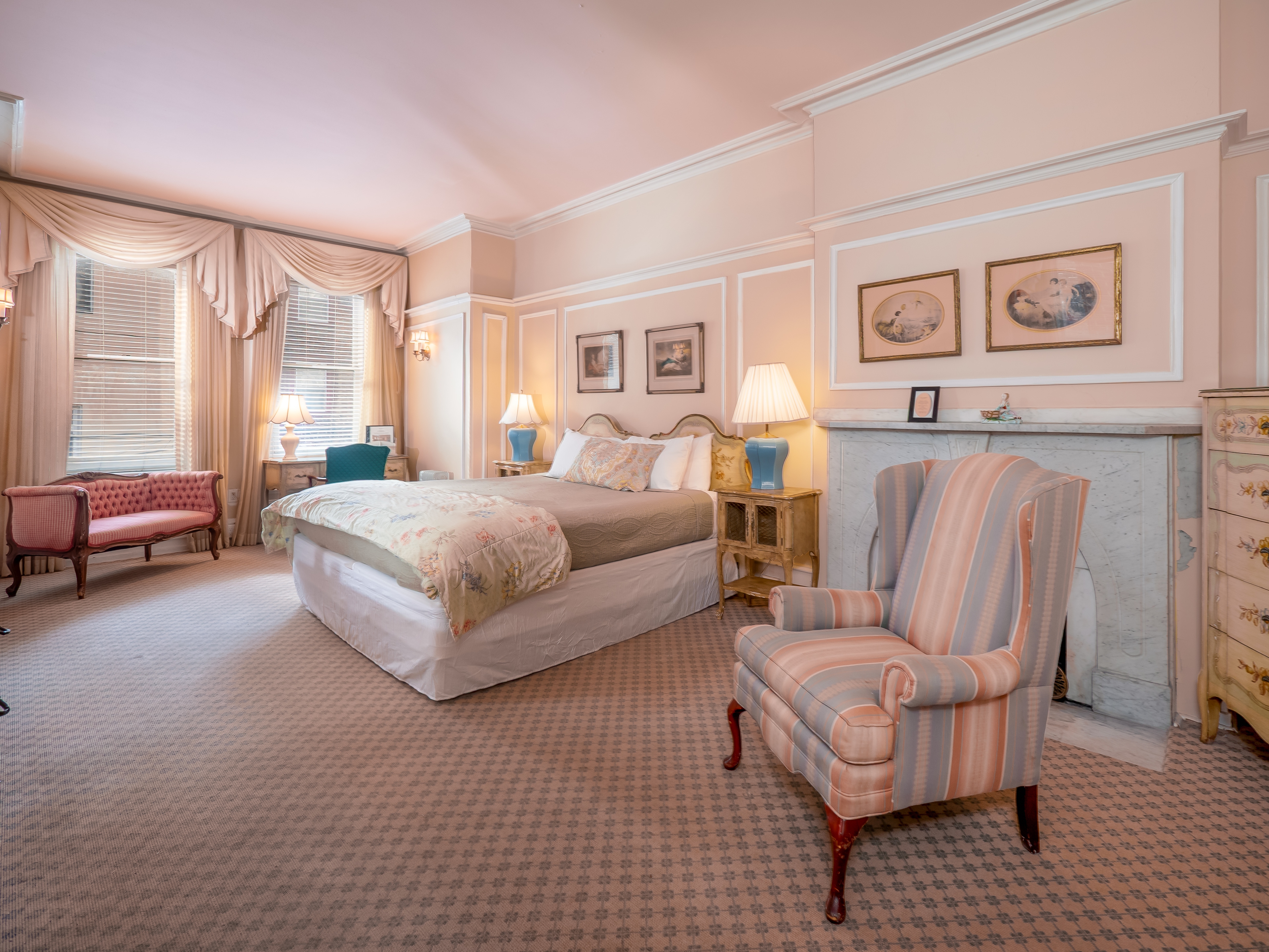 A calming bedroom suite with a queen bed, a decorative fireplace, loveseat and wall art.