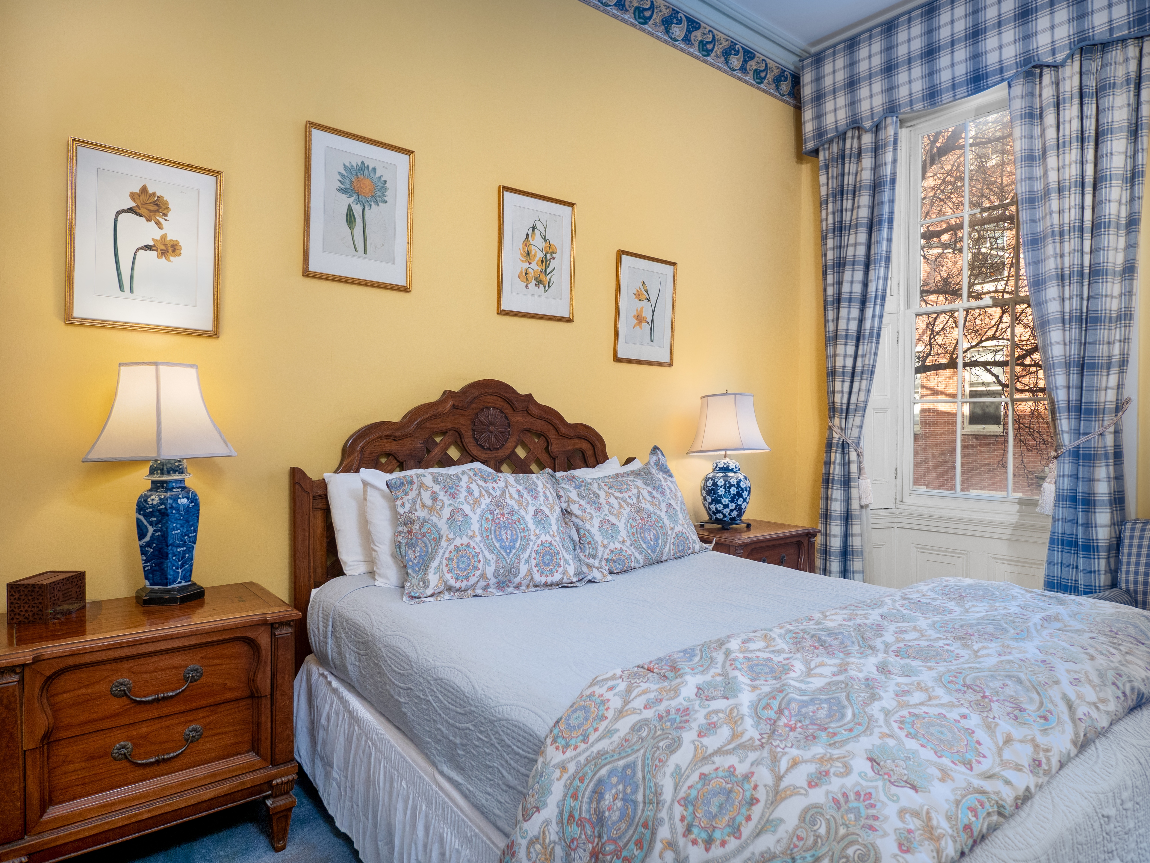 Close up of a bed that has two bedside tables with lamps on them. The window provides natural light.