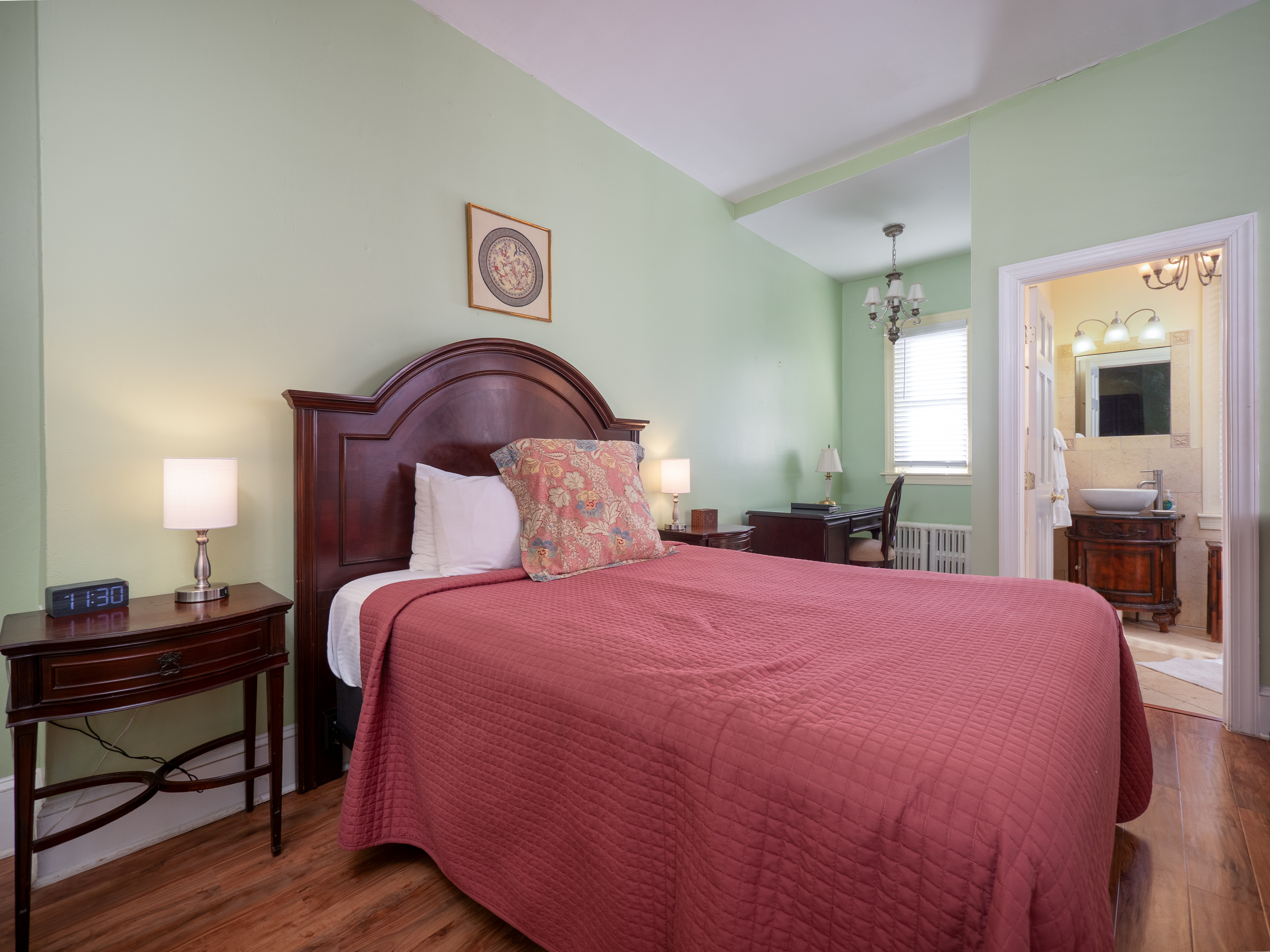 Close up of the queen bed with the desk area and bathroom entrance in behind it.