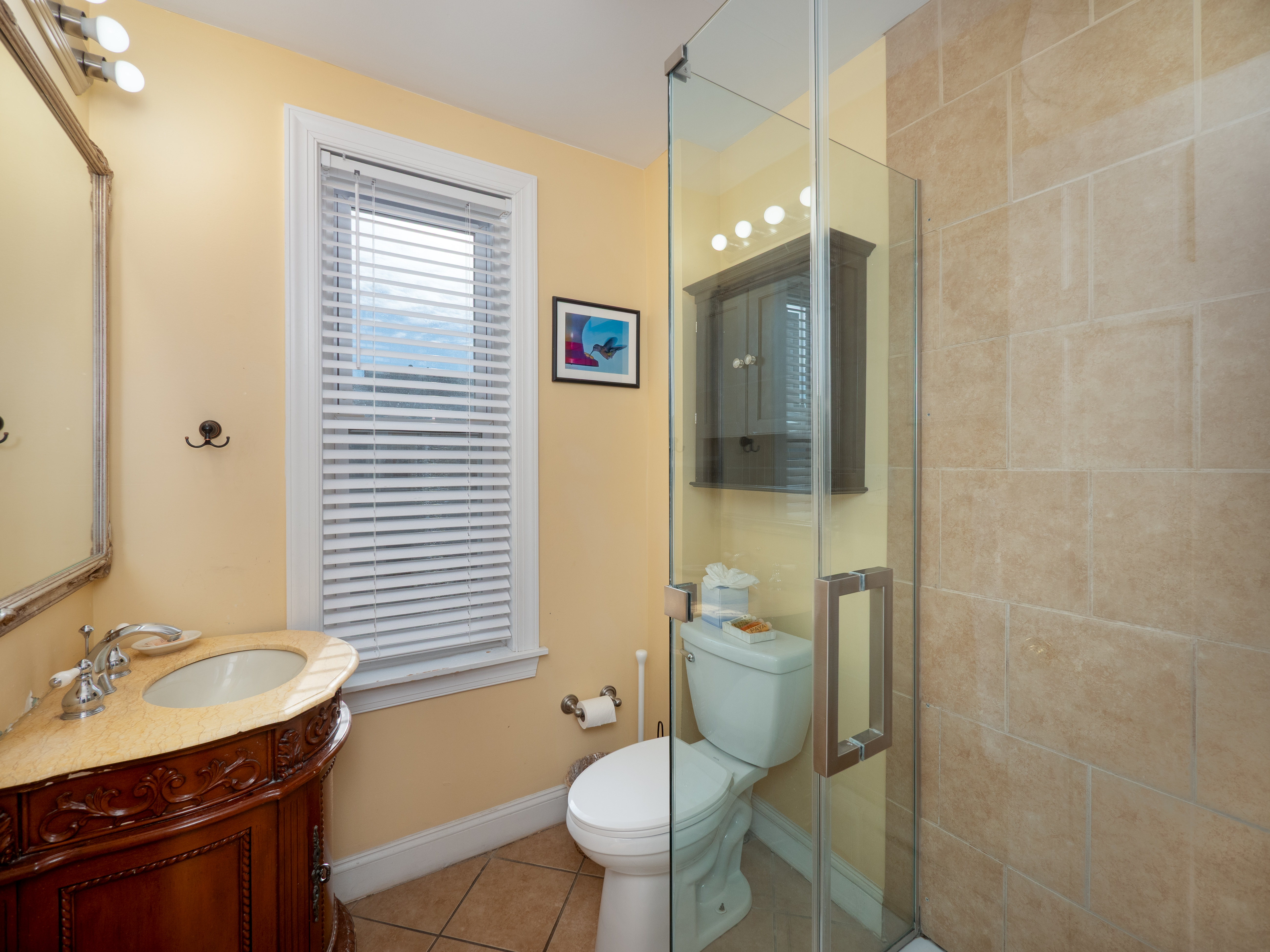 Full bathroom with a glass door standing shower. There is a window between the toilet and the sink.