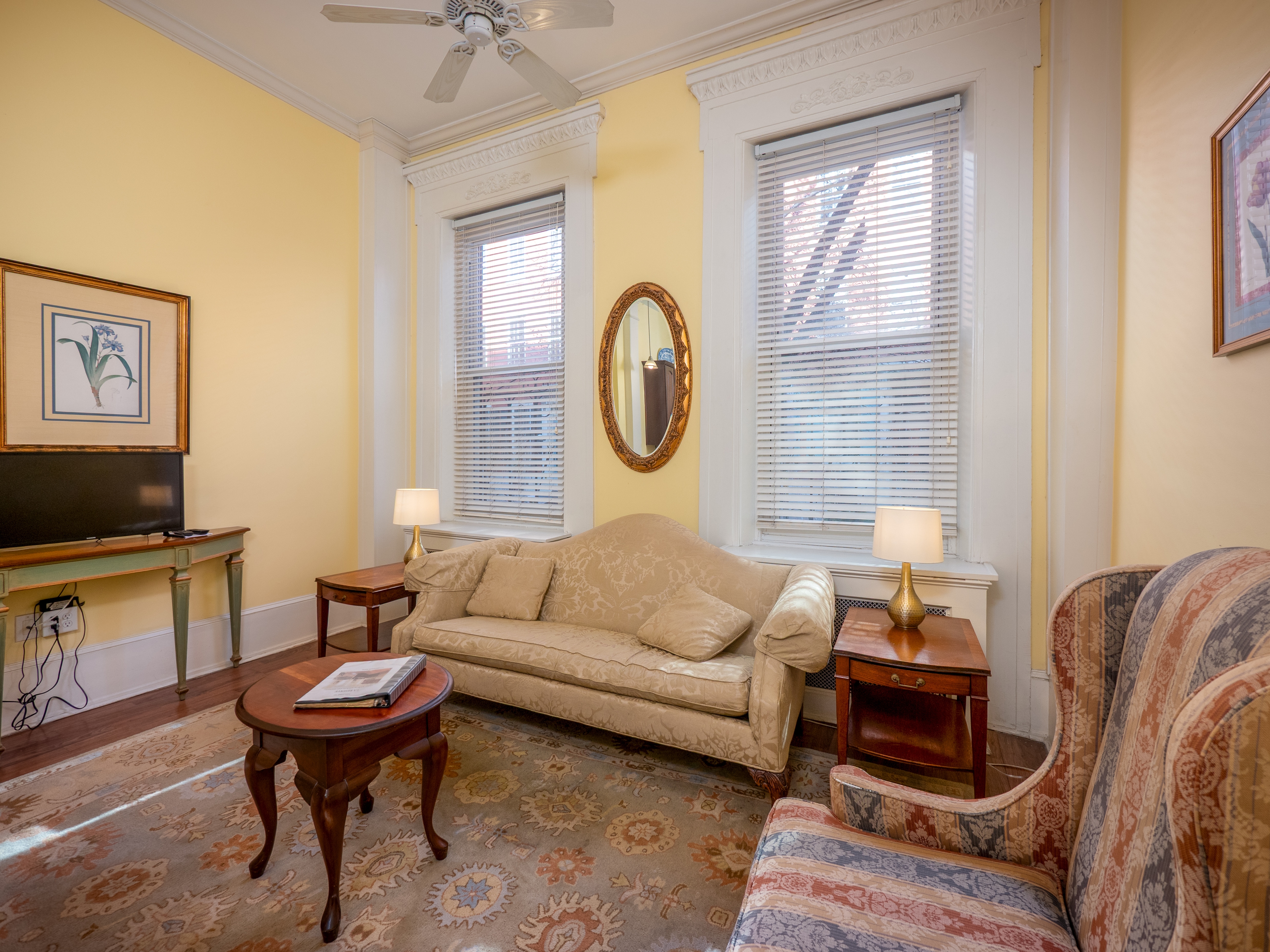 Comfortable sitting area with sofa, an armchair and end tables. There are windows providing natural light.