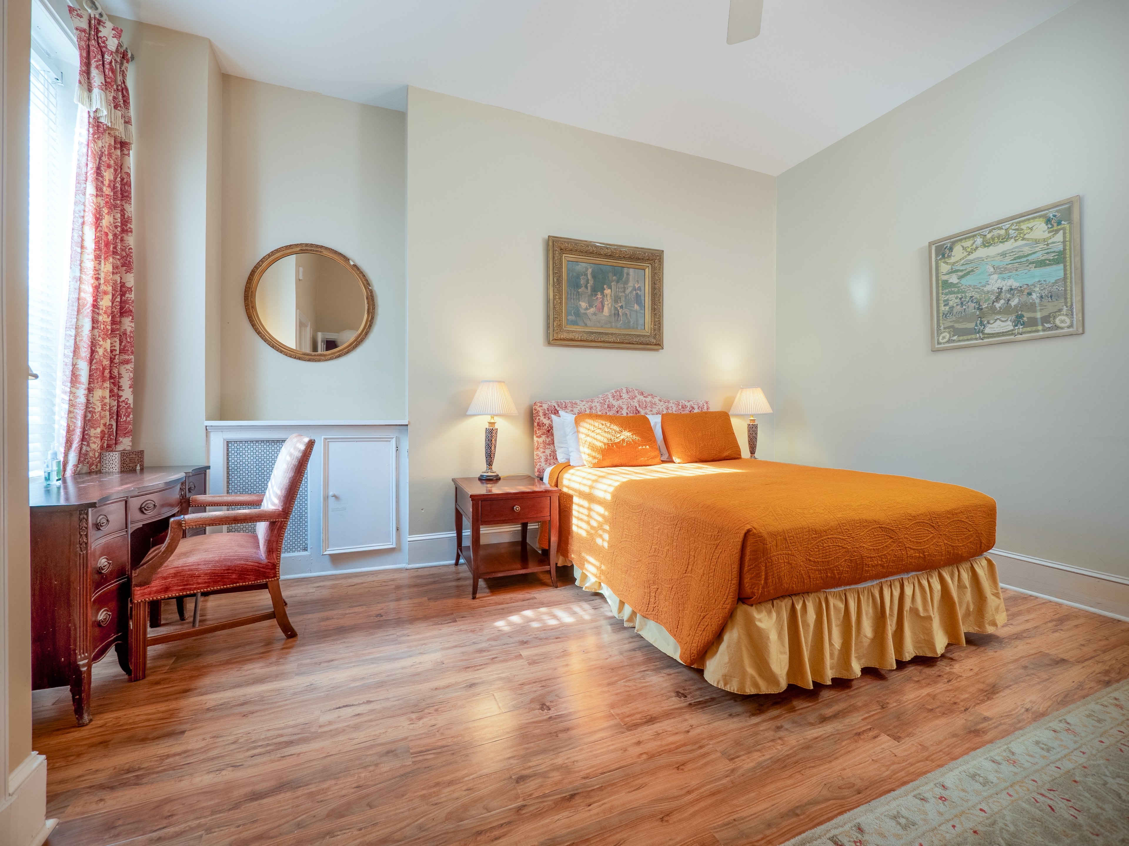 Dainty bedroom with a queen bed, desk facing the window providing natural light and two side tables with lamps on them.
