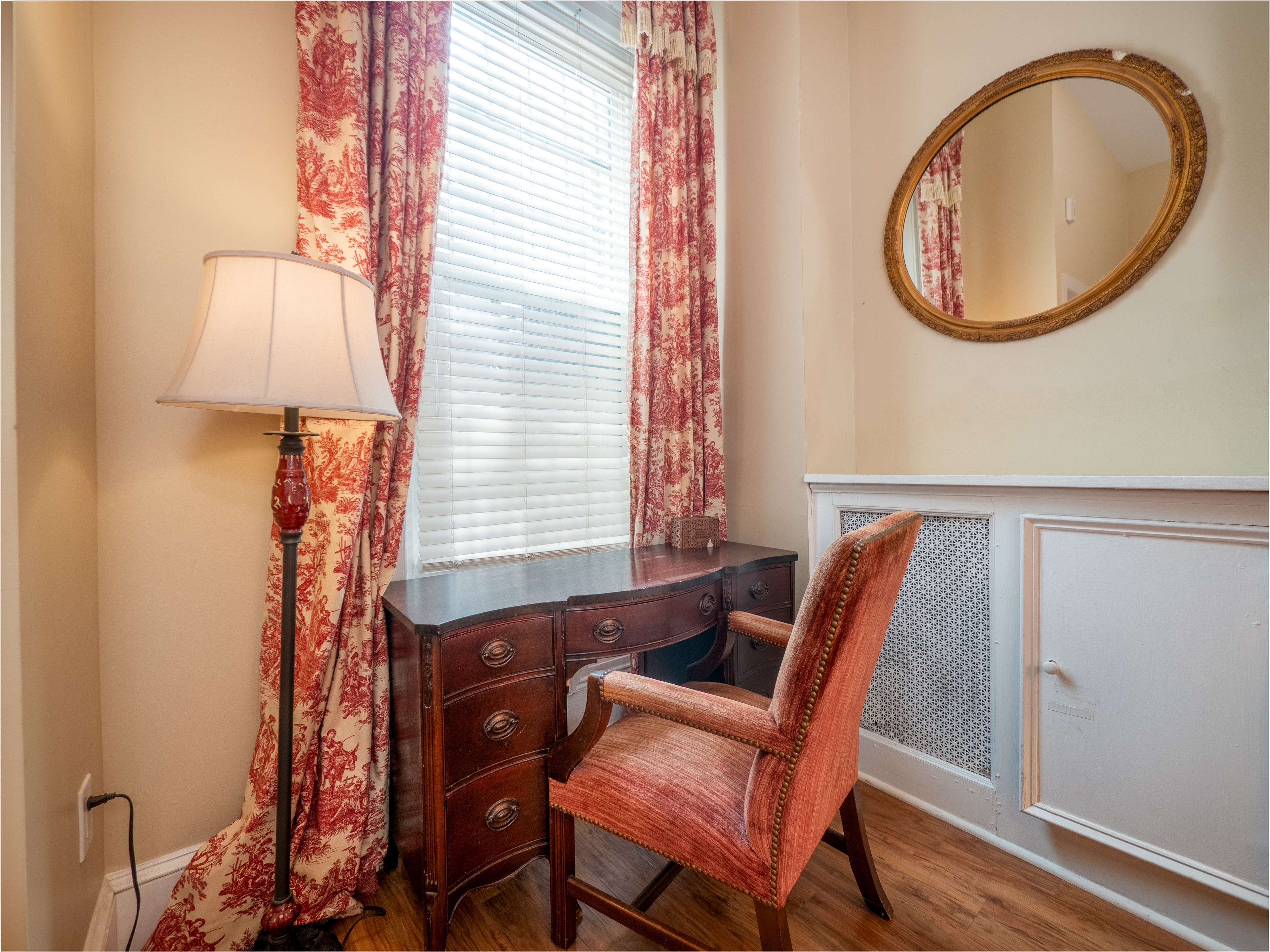 Close up of the desk and chair facing the window. A mirror and lamp are on either side of the desk.