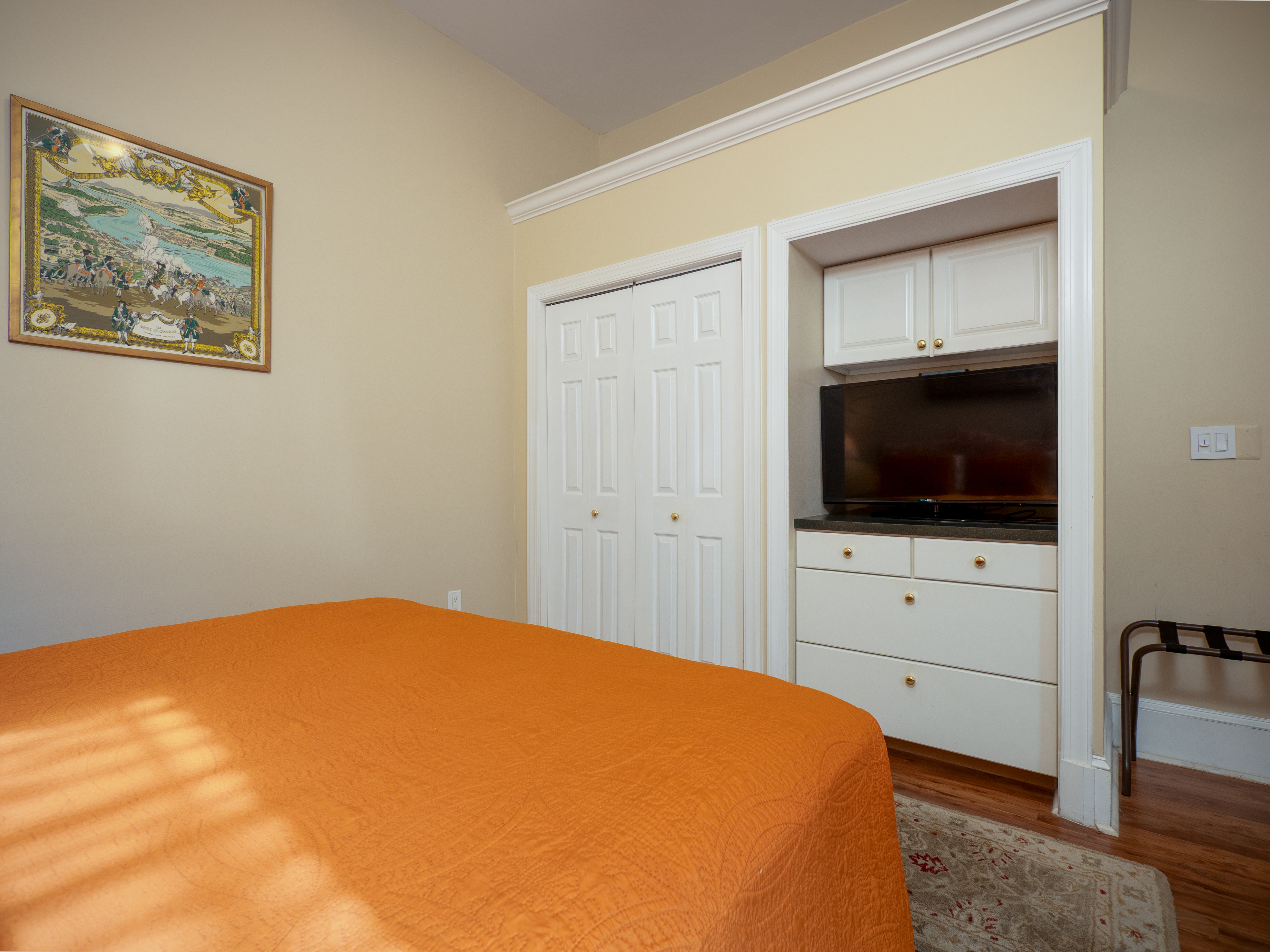 A TV in a cutout in the wall on a dresser sits across from the queen bed.