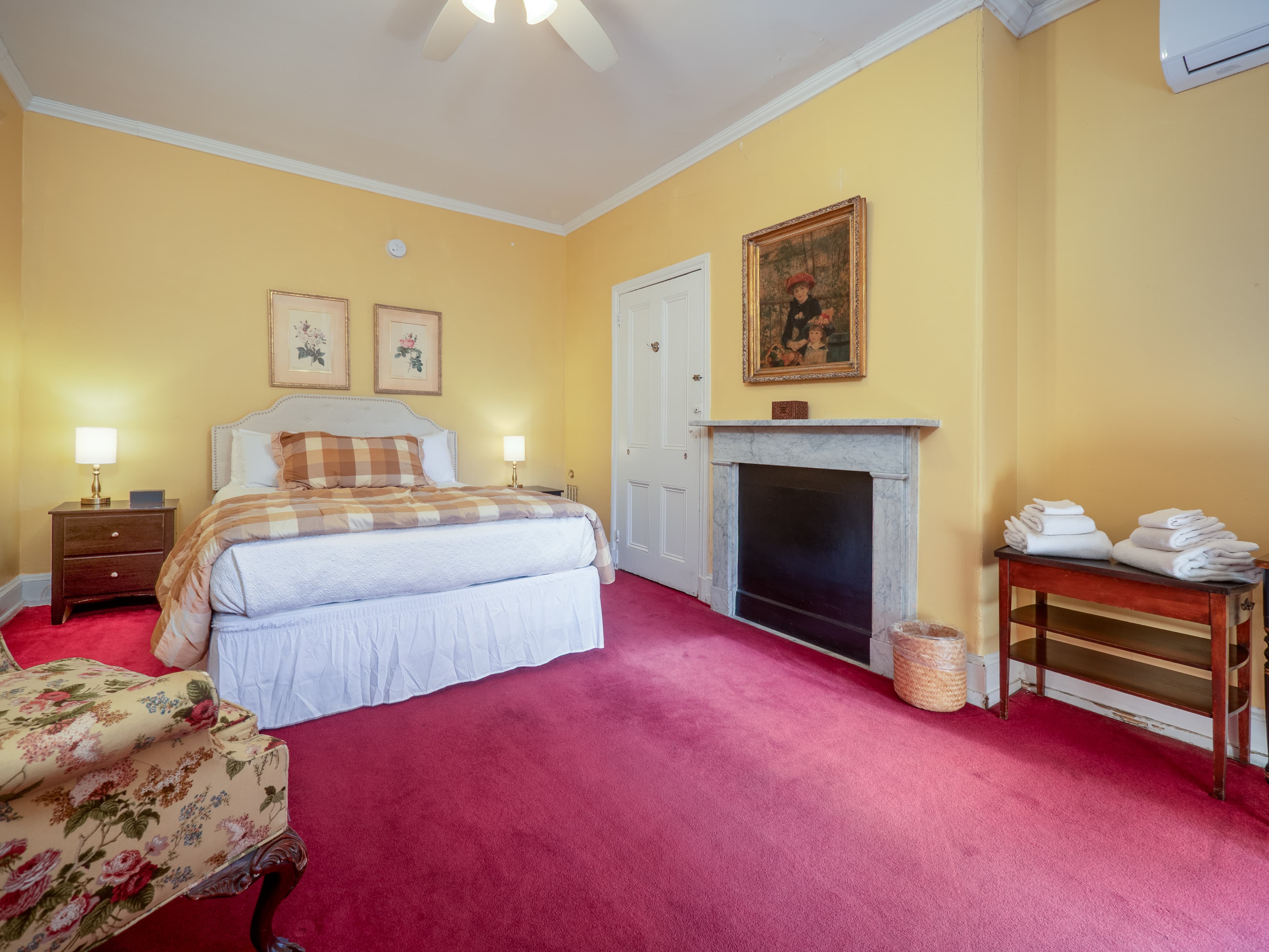 Vintage, carpeted bedroom with a queen sized bed, decorative fireplace, and sofa chair.
