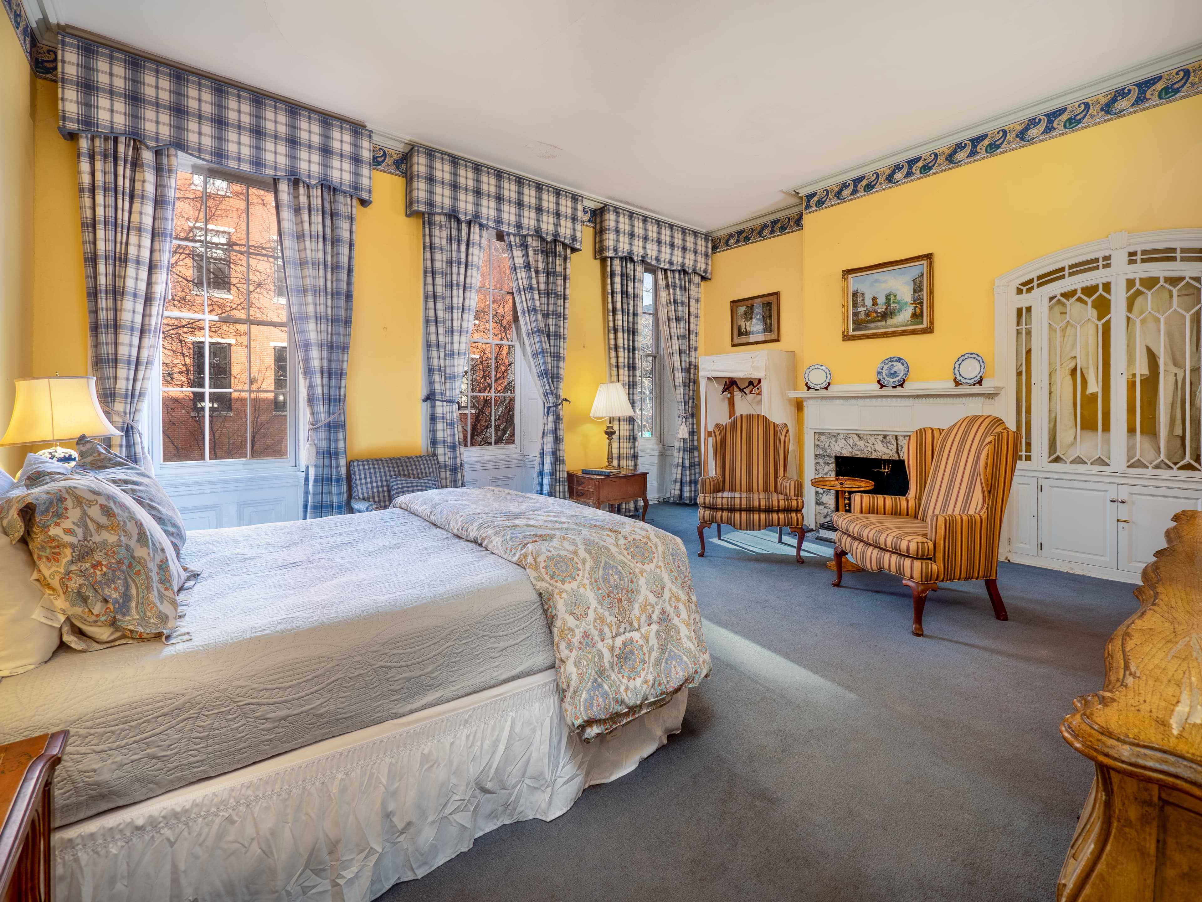 Lively bedroom with queen bed, three windows, matching armchairs, and a dresser.