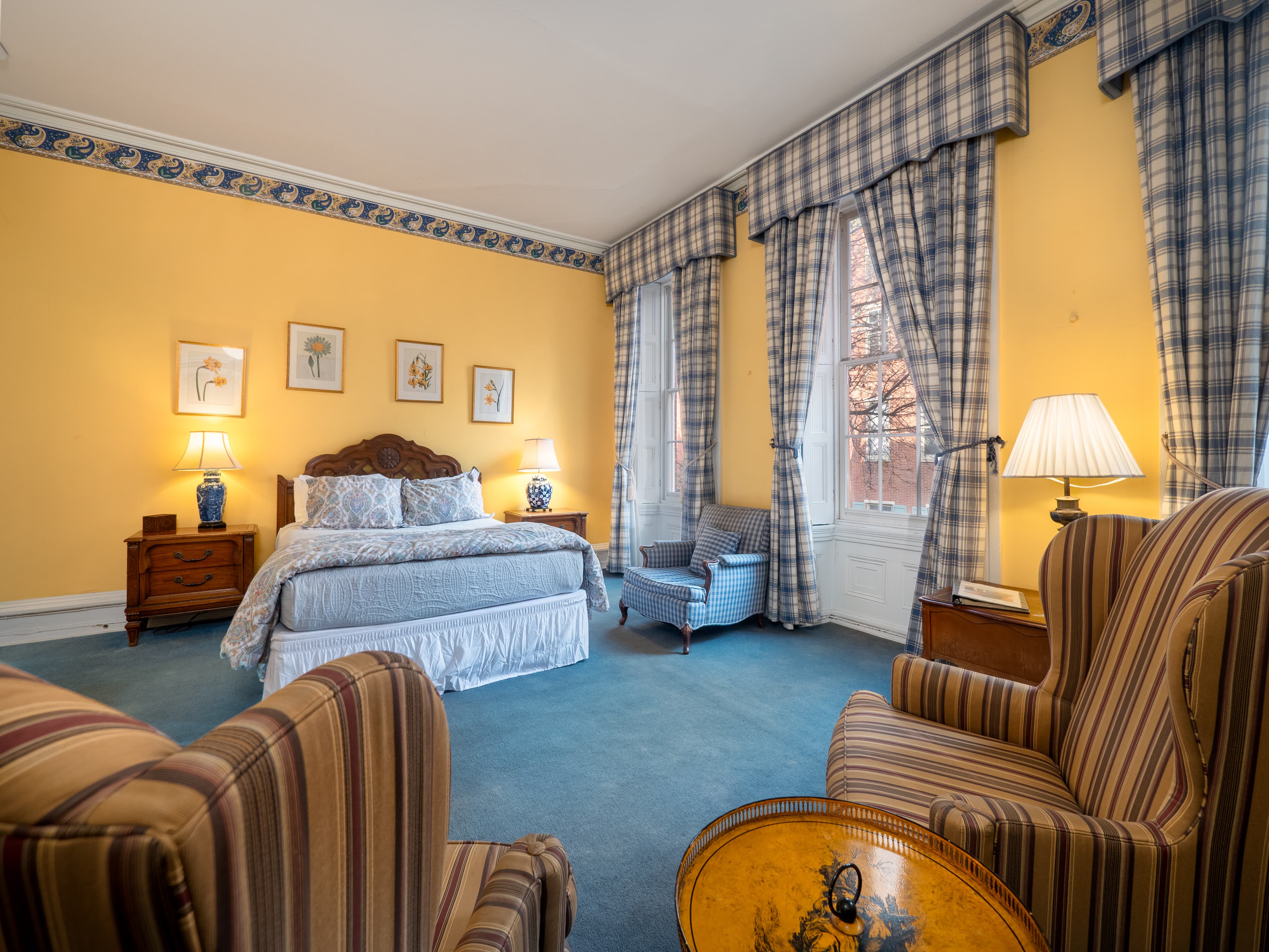 Queen bed from alternate view from behind the armchairs. The bed and windows are in the background.