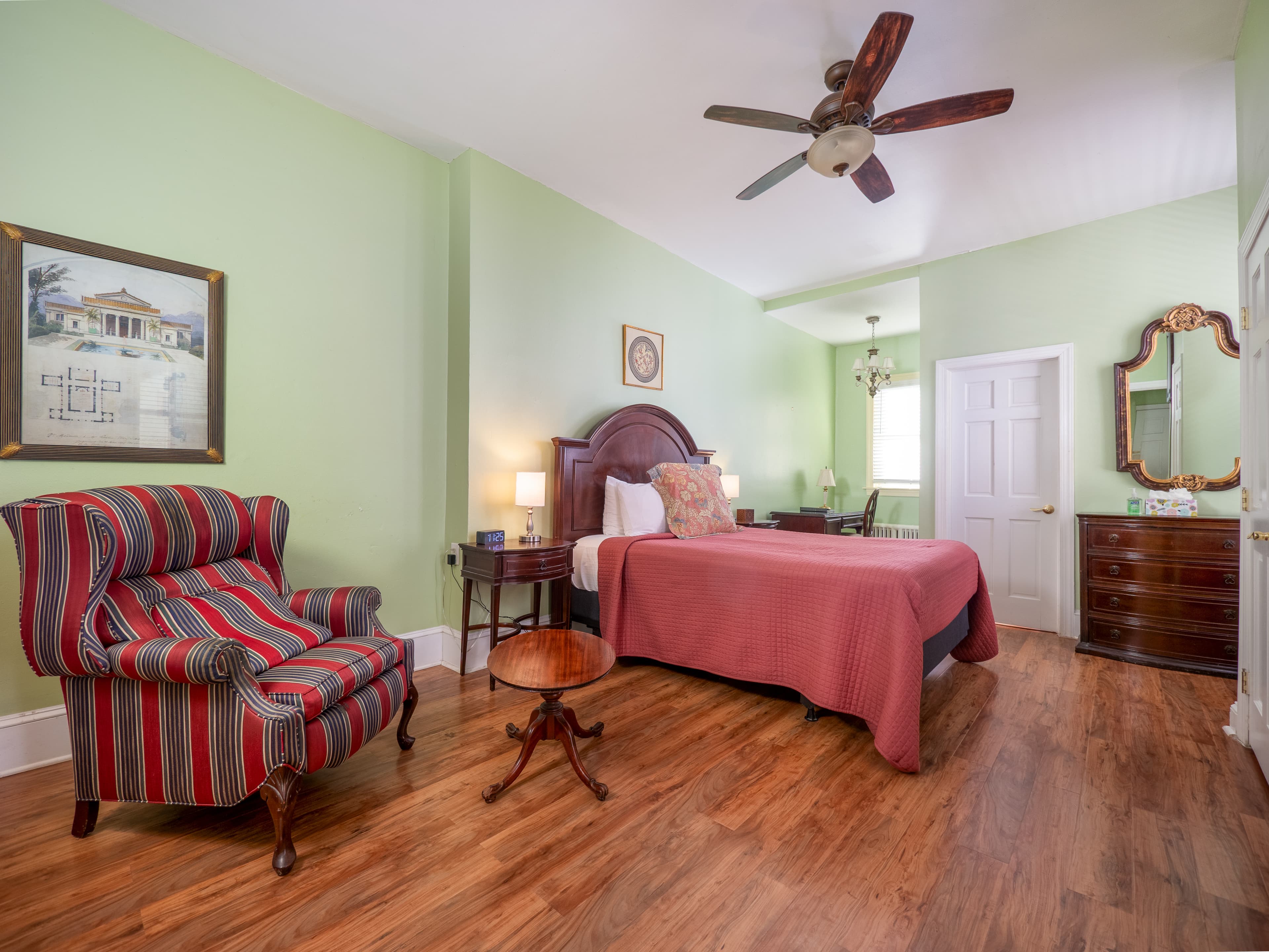 Cozy room with a queen bed, armchair, kitchenette, desk area and dresser.