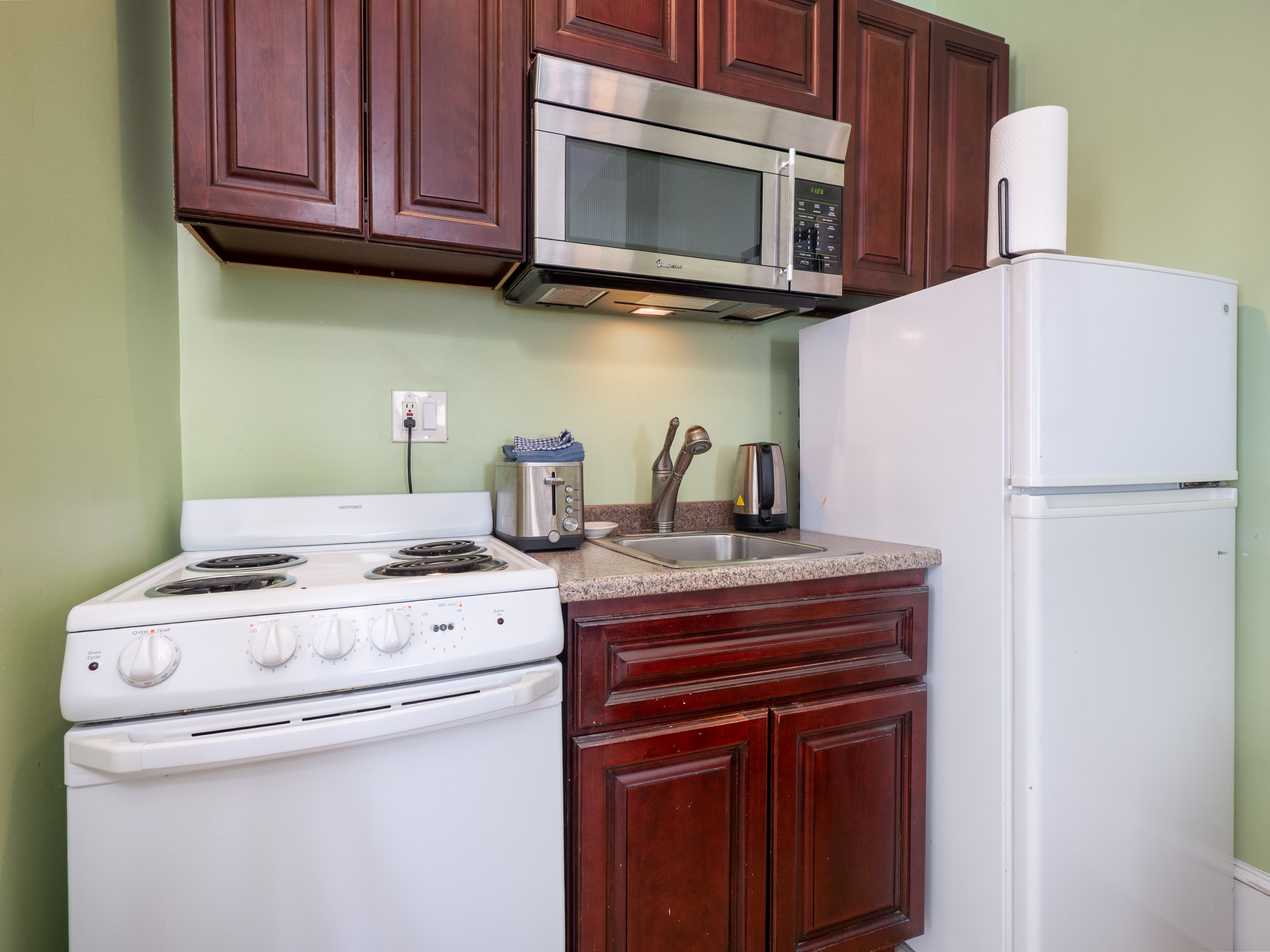 Closeup of the kitchenette that has a stove, sink, fridge, microwave and cabinets.