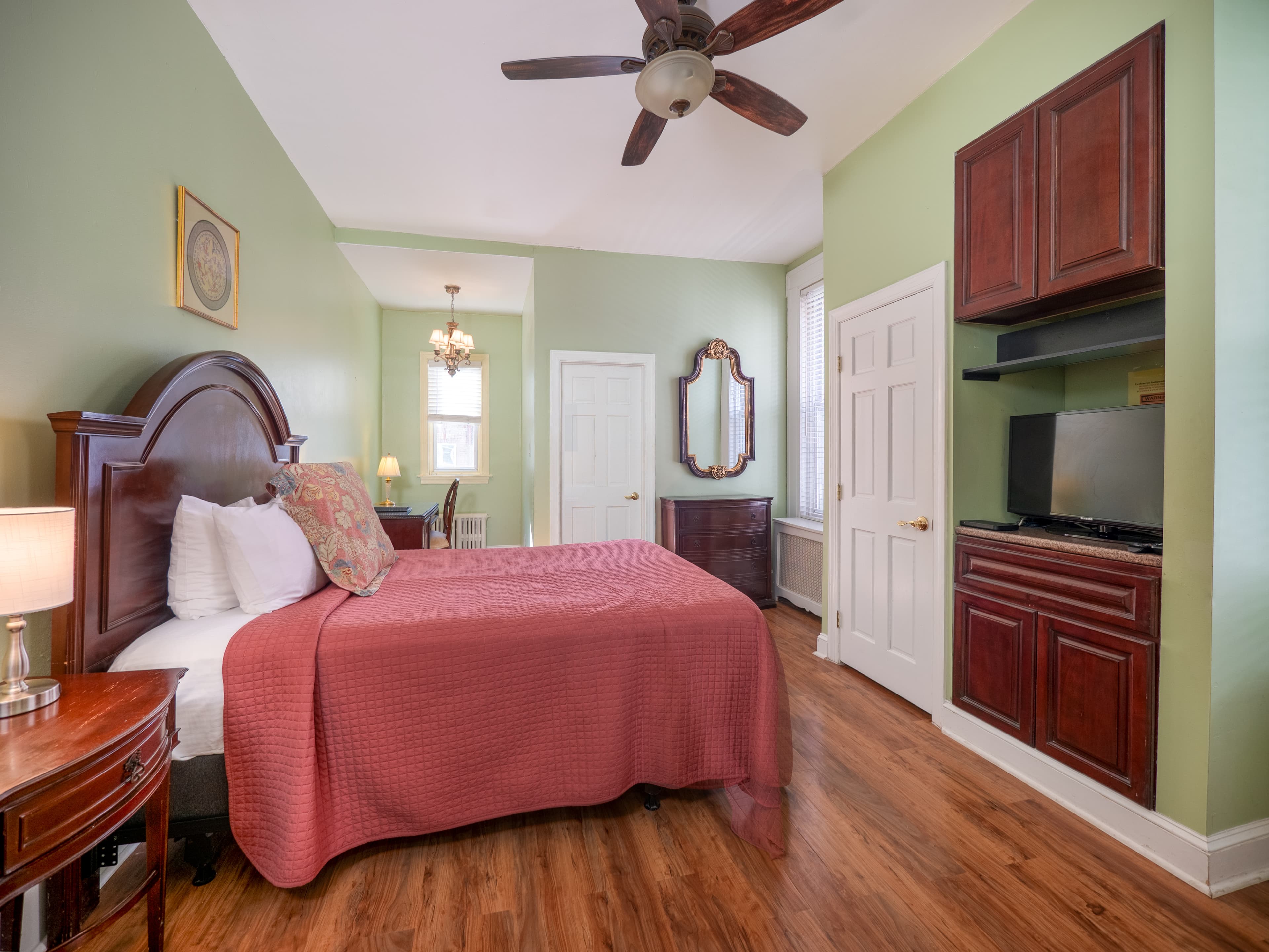 Alternate view of the bedroom showing a TV in the wall across from the bed with cabinets above it.