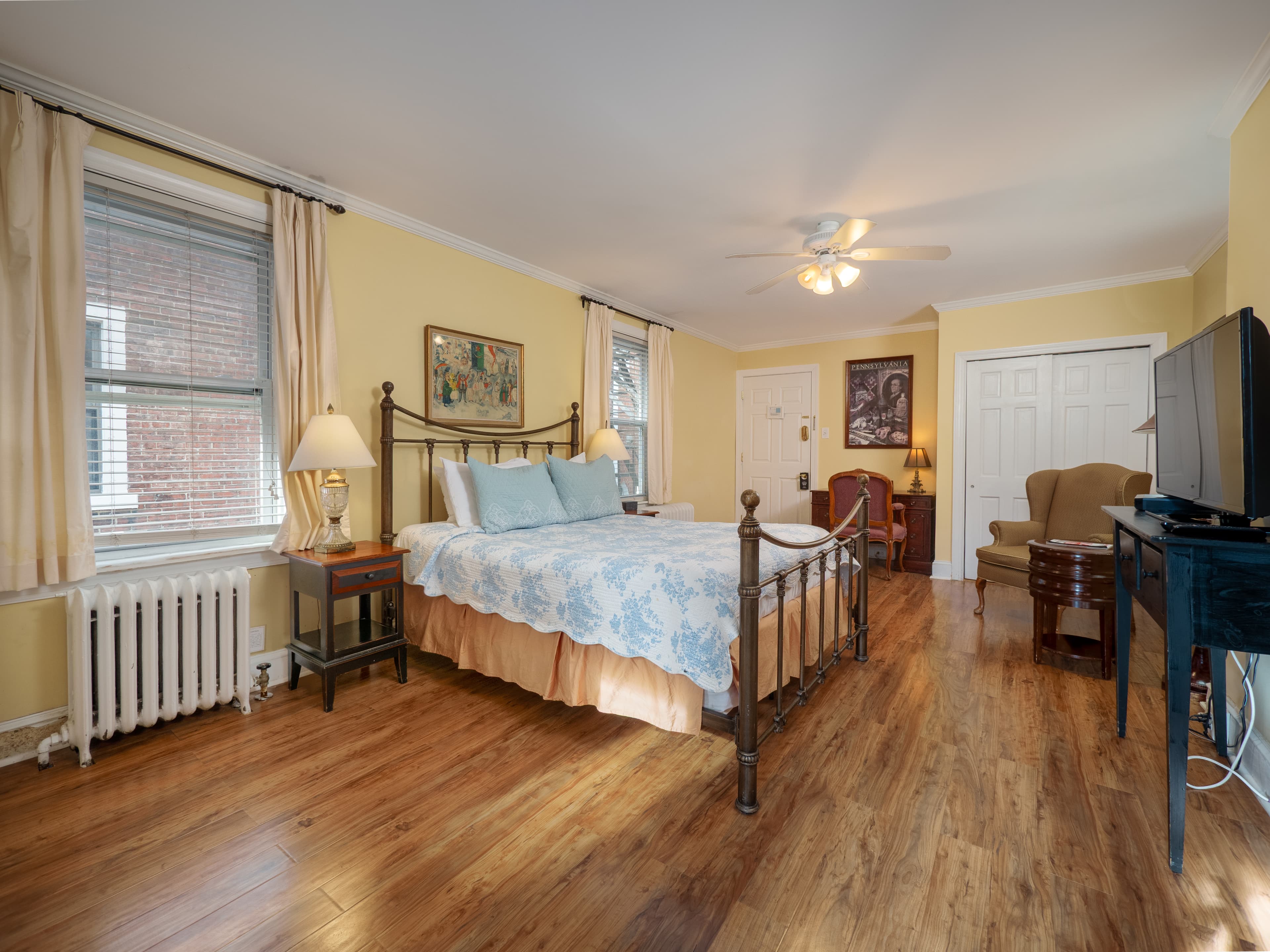 Alternate view of the bedroom facing the entrance. The TV sits across from the bed and a radiator sits below the window.