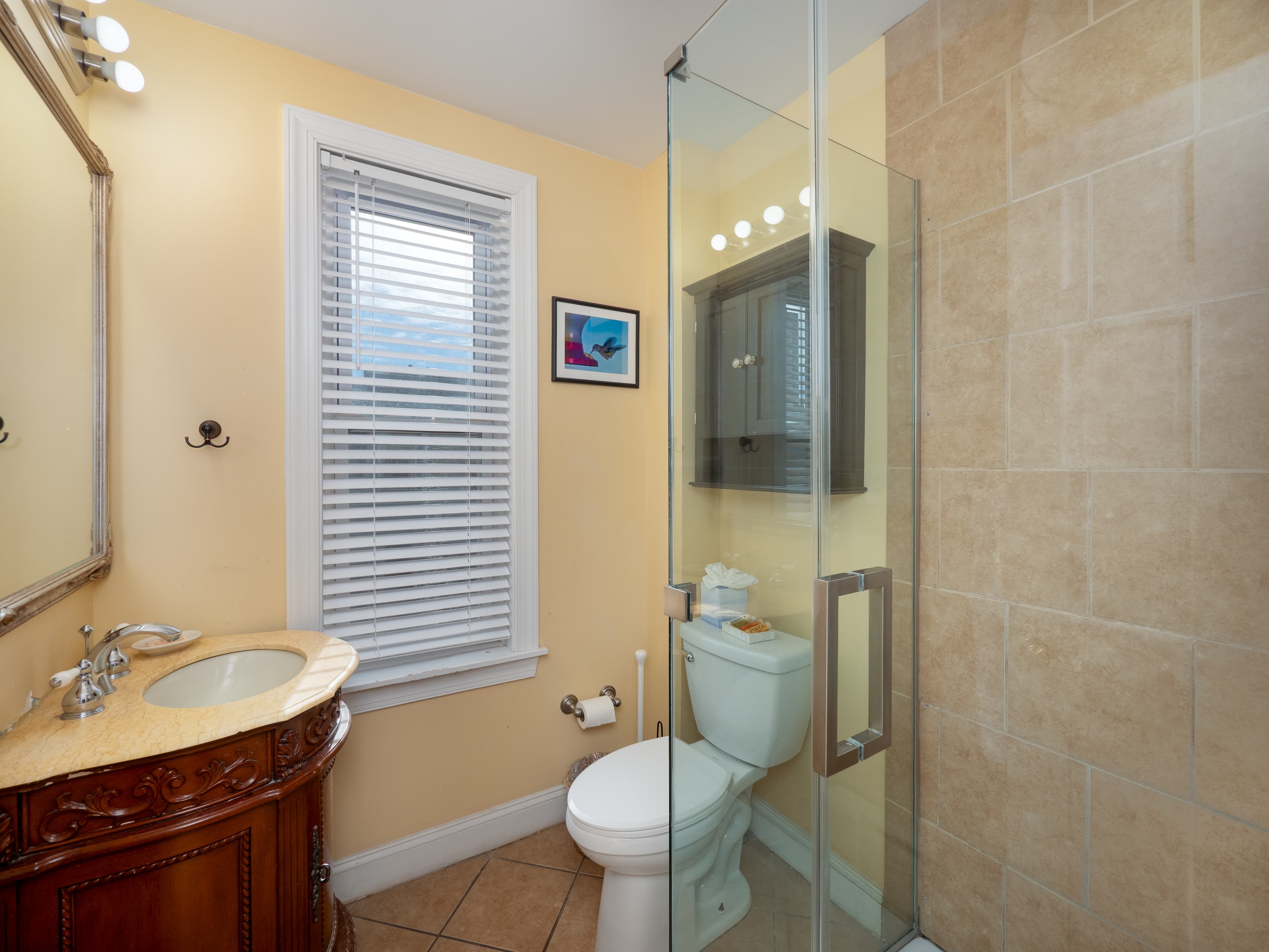 Full bathroom with a glass door standing shower. There is a window between the toilet and the sink.