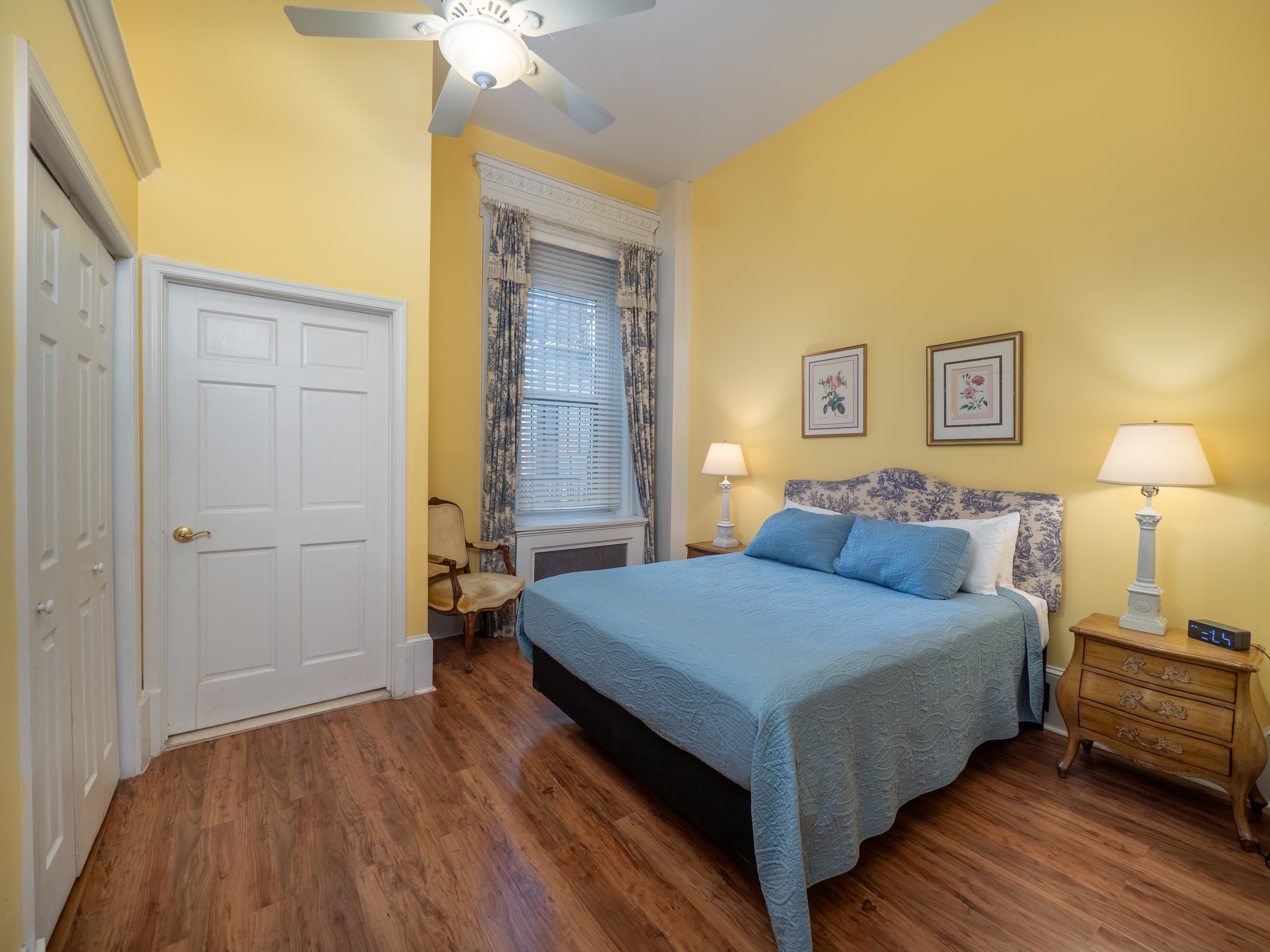 Calming bedroom with queen bed, closet, two side tables with lamps on them and a window providing natural light.