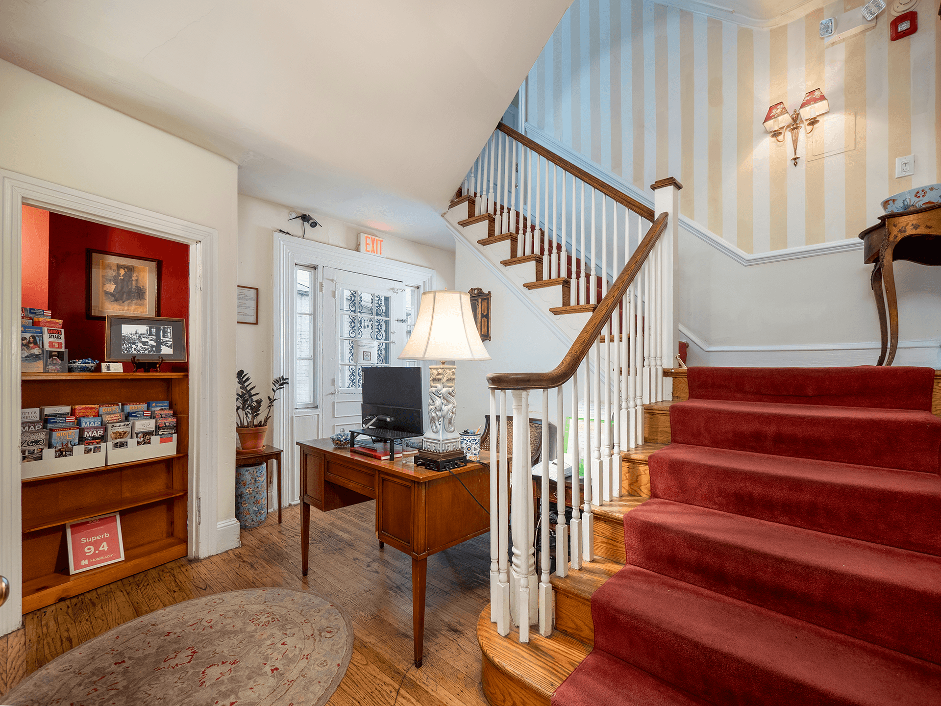 Interior view of a welcoming foyer featuring a staircase, desk with a lamp, and access to a front door.