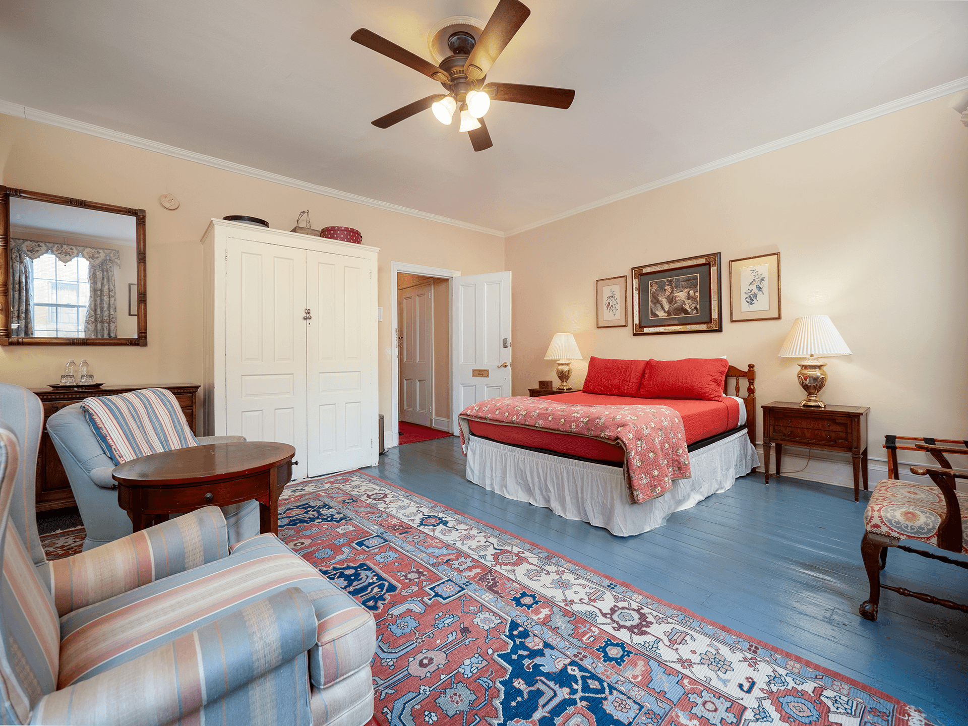 Cozy bedroom featuring a red bedspread, wooden furniture, and a patterned rug.