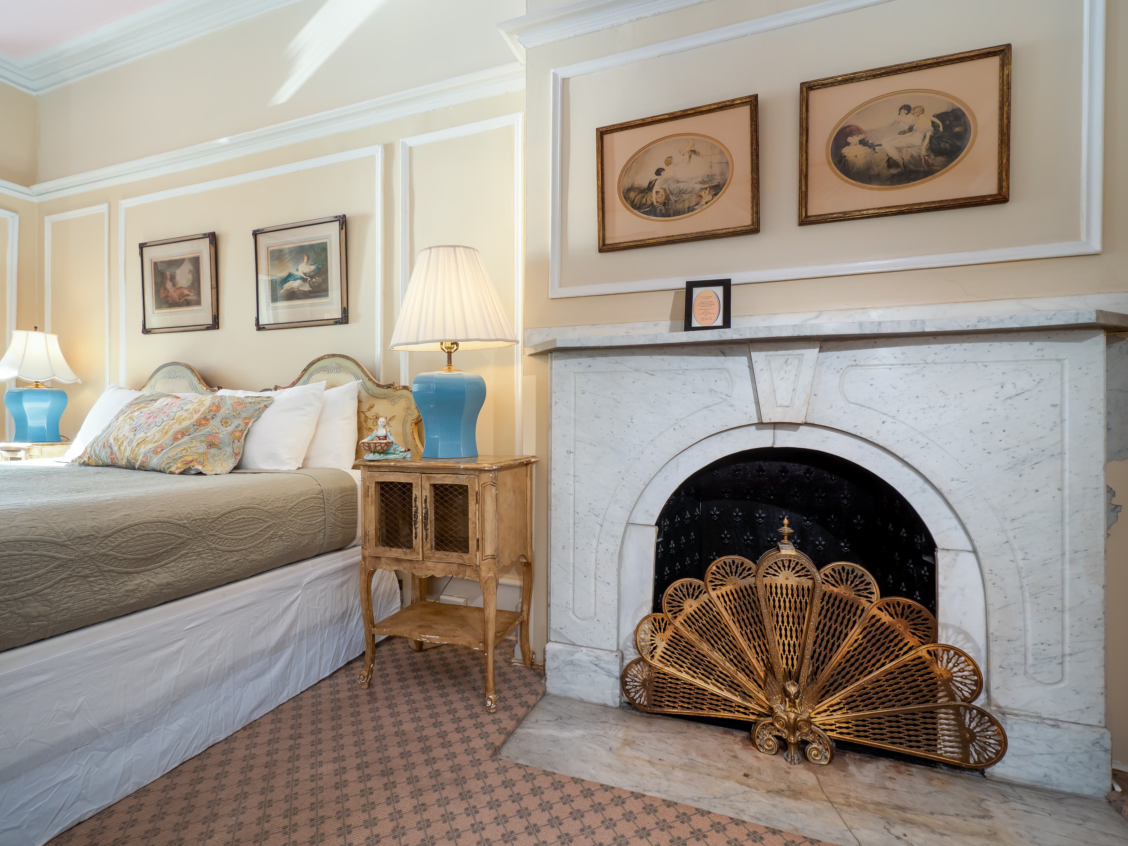A cozy bedroom featuring a bed, bedside table with a lamp, and a decorative fireplace with an intricate screen.