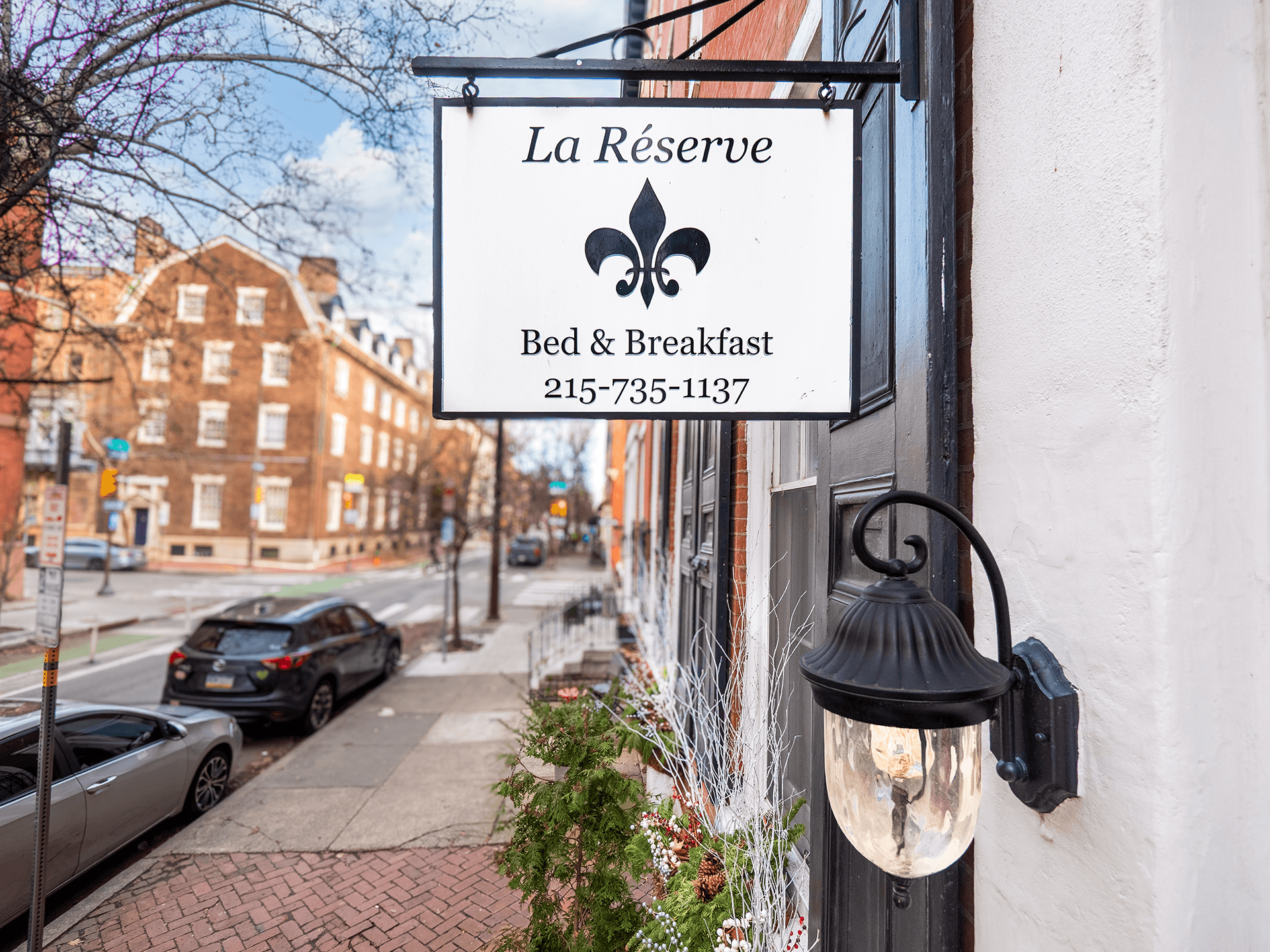 Sign for "La Réserve" Bed & Breakfast featuring a wrought iron lantern and a view of the street.