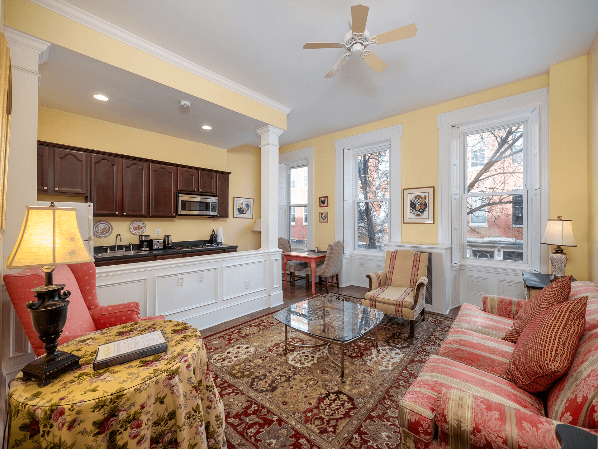 Cozy living space featuring a yellow wall, patterned furniture, and a kitchen area with wooden cabinets.